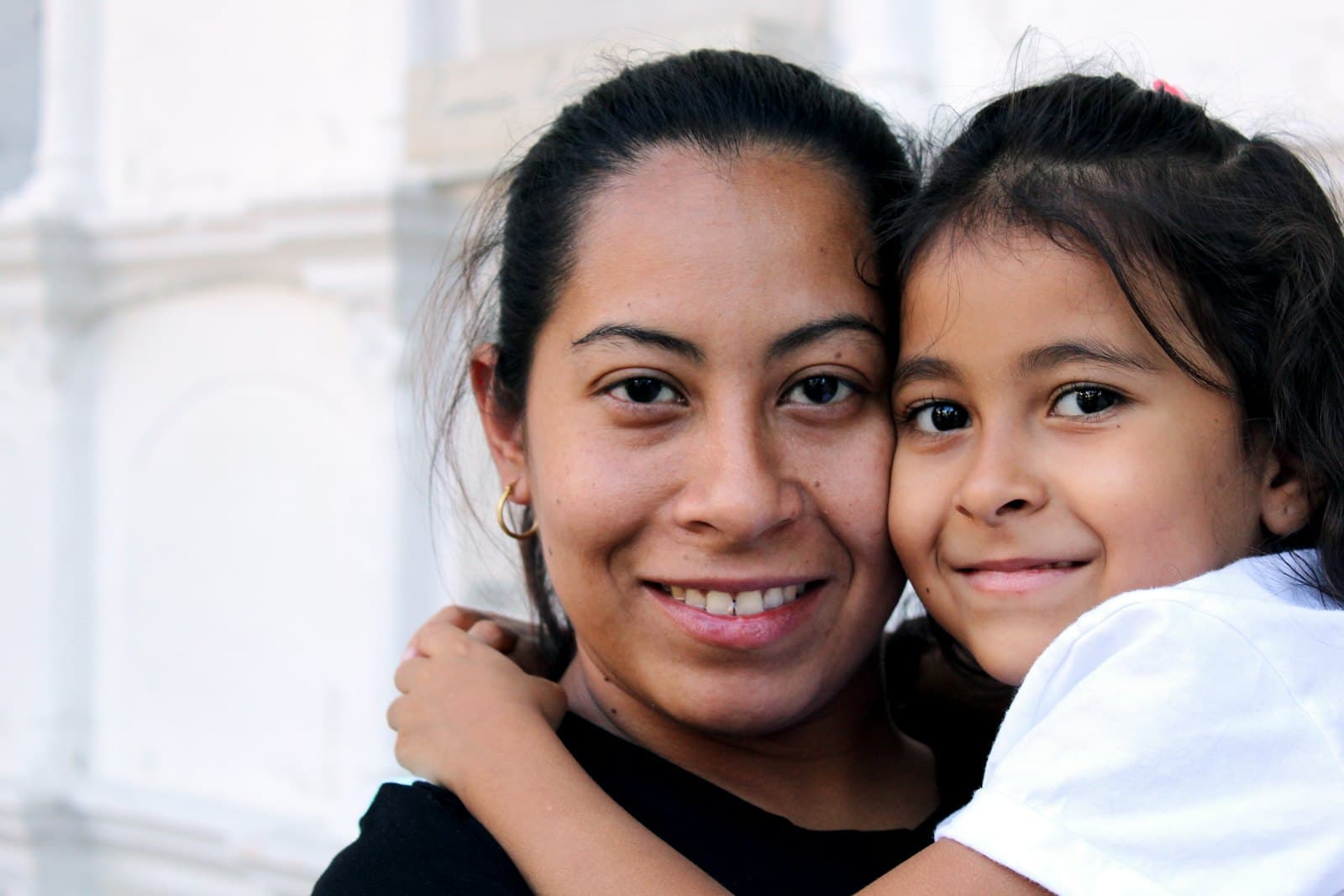 A mother and her young daughter, cheek to cheek, smiling at the camera